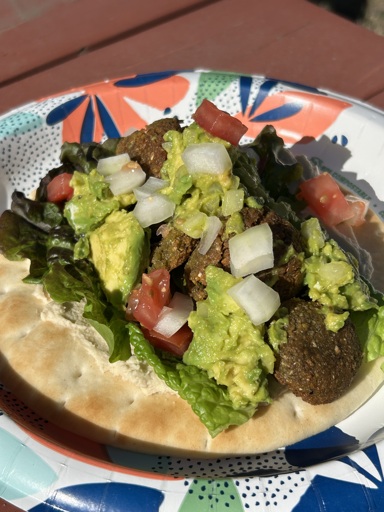 A falafel wrap on pita bread piled high with hummus, lettuce, falafel balls, guacamole, onions and tomatoes. 