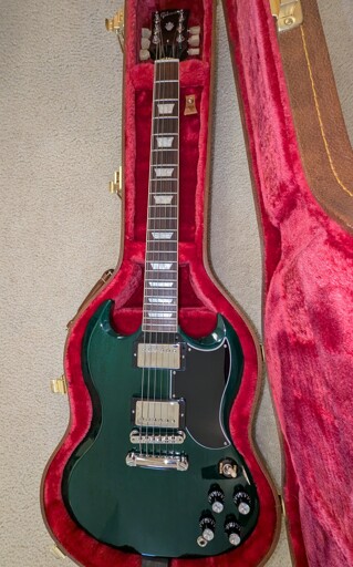 A Gibson SG guitar with green body in a brown hard shell case with a plush red interior.