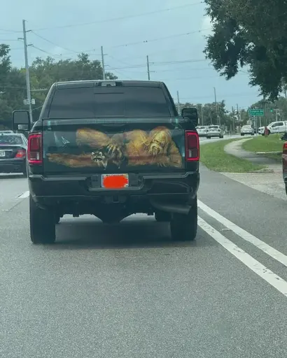 A photo of a Tampa-area pickup truck with a bigfoot stroking a raccoon painted on its tailgate, painted in a manner to pretend the tailgate is transparent and those are the contents of the truck bed